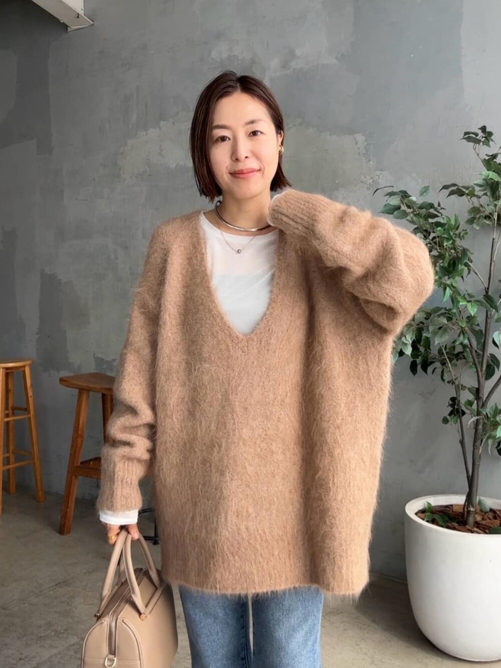 イエロー系のニット/セーター、ブルー系のデニムパンツ、ベージュ系のボストンバッグを着用したレディースの秋コーディネートの4枚目の写真