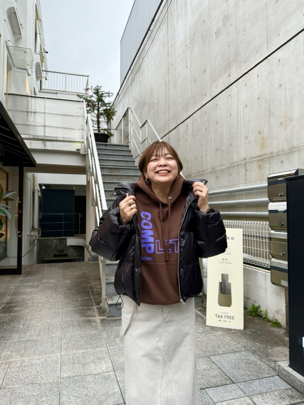 ブラック系のダウンジャケット/コート、グレー系のデニムスカート、ブラウン系のパーカーを着用したレディースの秋コーディネートの2枚目の写真