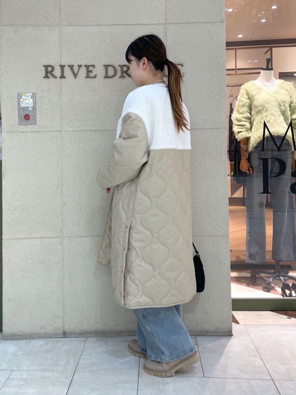 ベージュ系のダウンジャケット/コート、ブルー系のデニムパンツ、ブラック系のショルダーバッグを着用したレディースの秋コーディネートの2枚目の写真