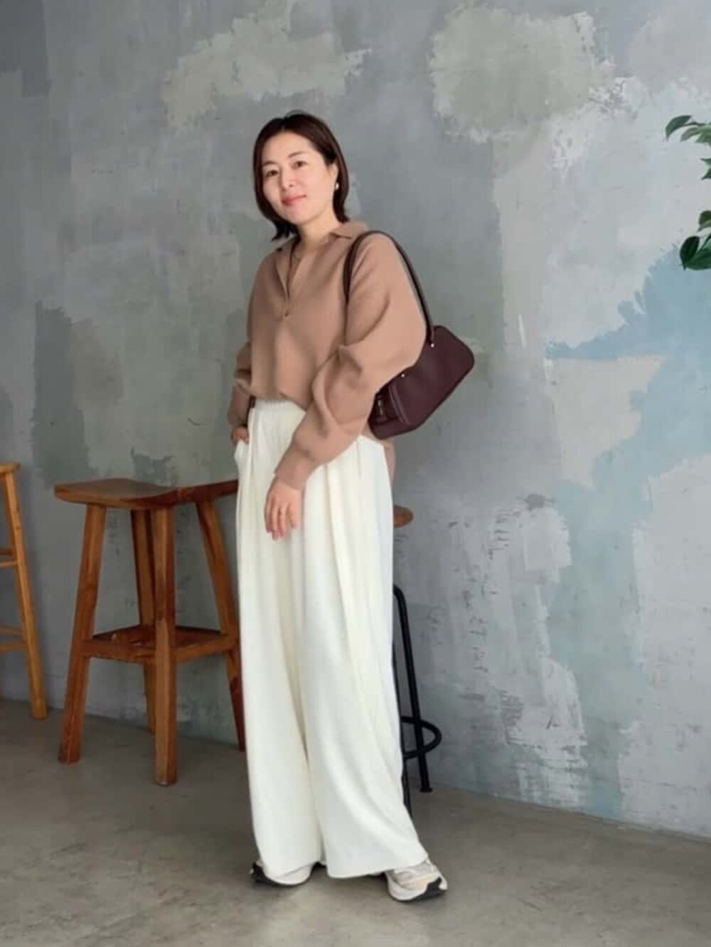 イエロー系のニット/セーター、ブラウン系のショルダーバッグ、ホワイト系のスラックスを着用したレディースの冬コーディネートの2枚目の写真