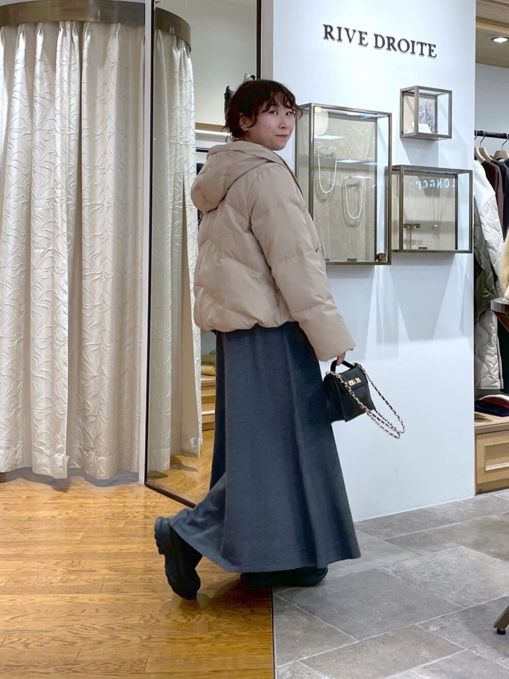 ブラック系のダウンジャケット/コート、グレー系のワンピース、ブラック系のブーツを着用したレディースの冬コーディネートの3枚目の写真