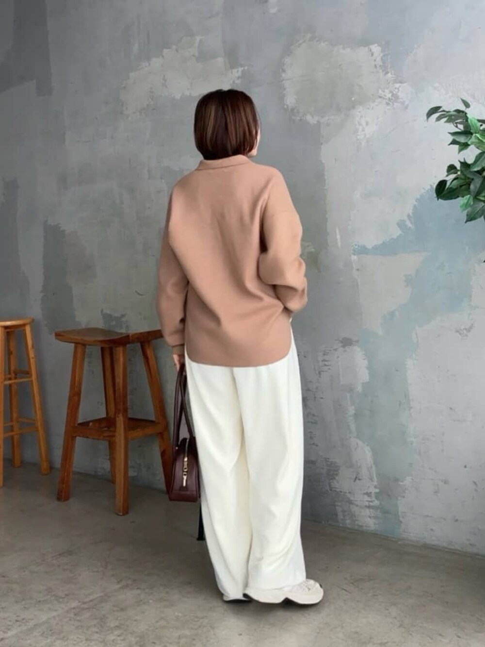 イエロー系のニット/セーター、ブラウン系のショルダーバッグ、ホワイト系のスラックスを着用したレディースの冬コーディネートの3枚目の写真