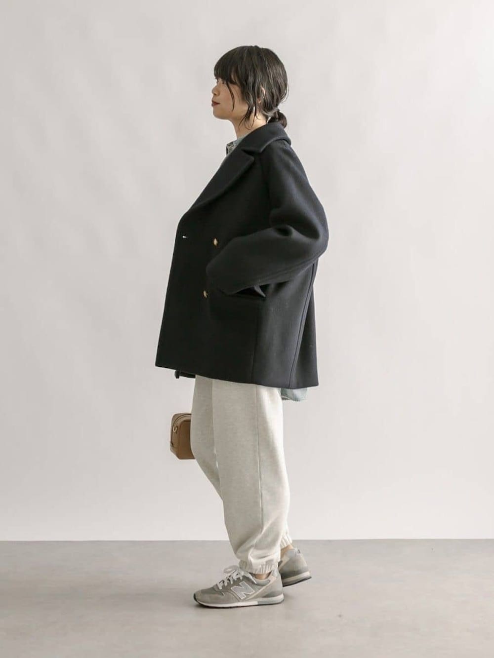 グレー系のスウェットパンツ、イエロー系のボストンバッグ、ブルー系のピーコートを着用したレディースの冬コーディネートの2枚目の写真