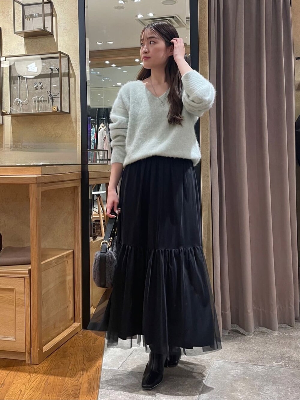 グリーン系のニット/セーター、ブラック系のスカート、ブラック系のブーツを着用したレディースの冬コーディネートの2枚目の写真