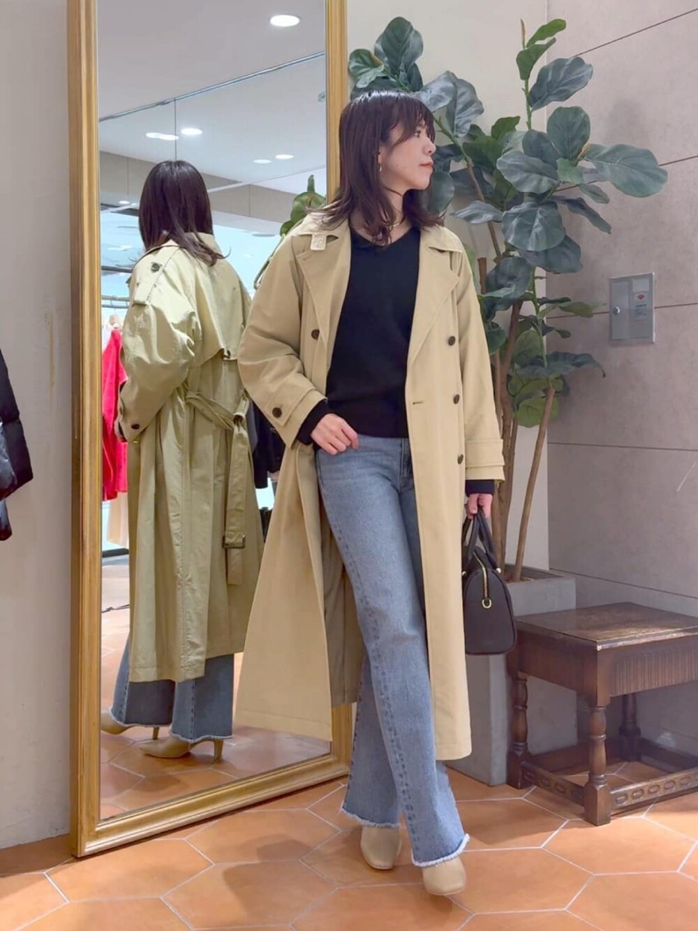 ベージュ系のトレンチコート、ブラック系のボストンバッグ、ブルー系のデニムパンツを着用したレディースの冬コーディネートの2枚目の写真