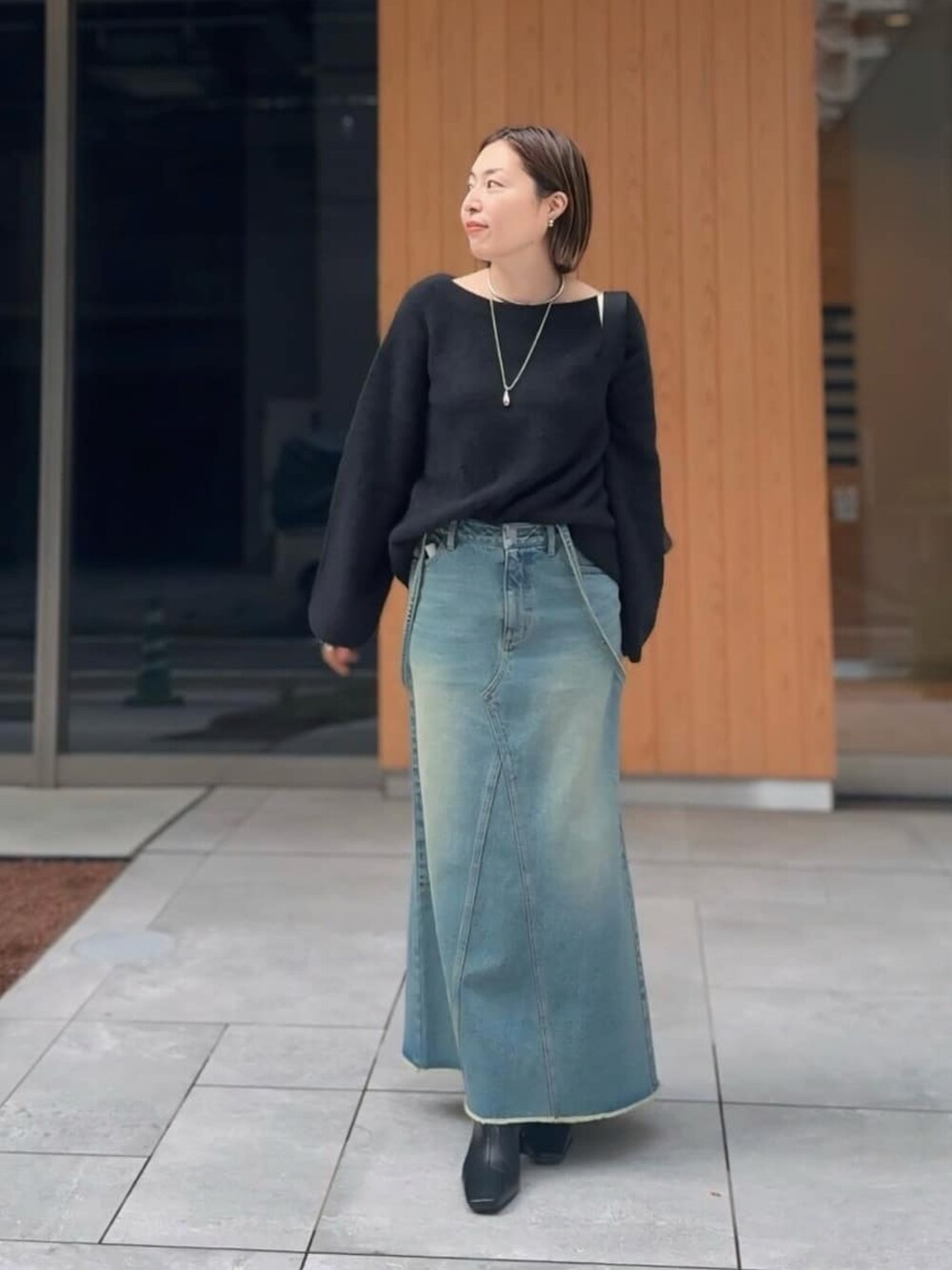 ブルー系のデニムスカート、ブラック系のニット/セーター、ブラック系のブーツを着用したレディースの秋コーディネートの2枚目の写真