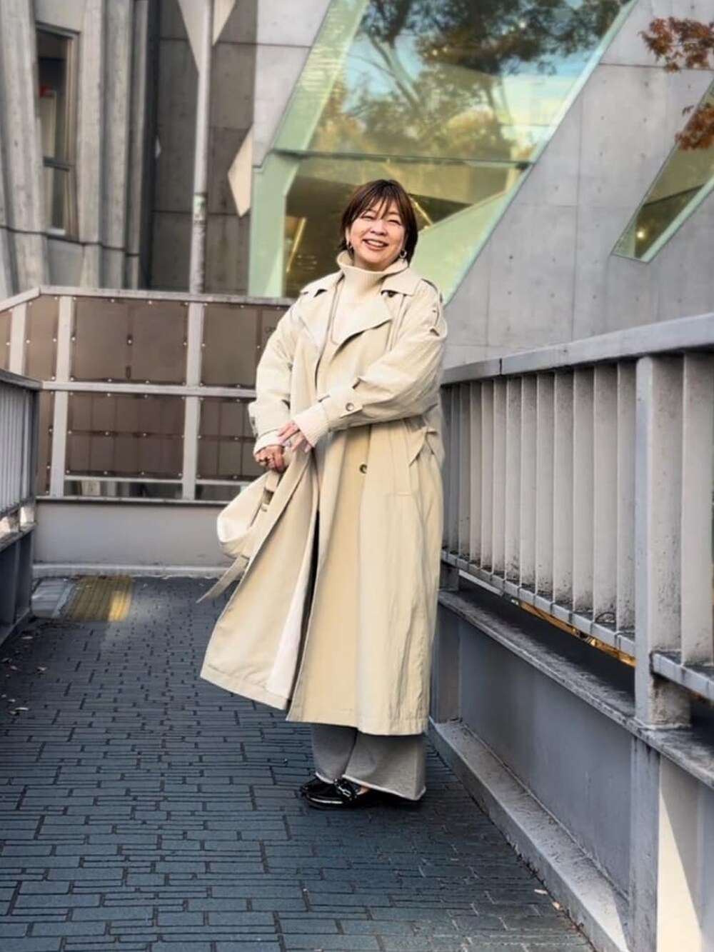 ホワイト系のニット/セーター、ベージュ系のトレンチコート、グレー系のスウェットパンツを着用したレディースの秋コーディネートの2枚目の写真