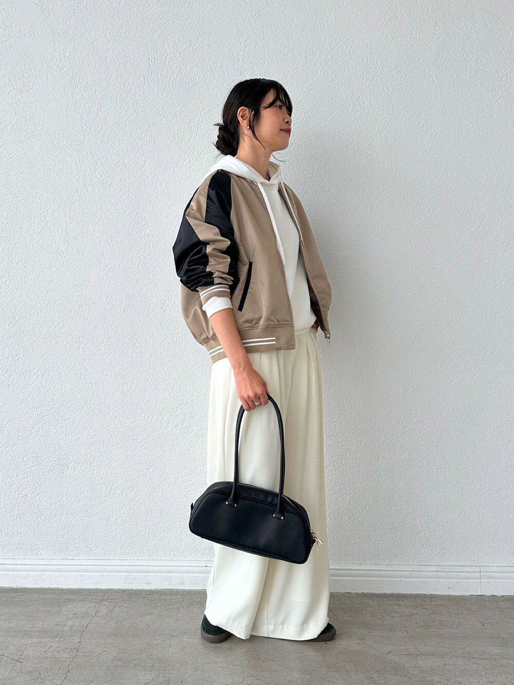 ホワイト系のスラックス、ブラック系のショルダーバッグ、ベージュ系のブルゾンを着用したレディースの夏コーディネートの2枚目の写真