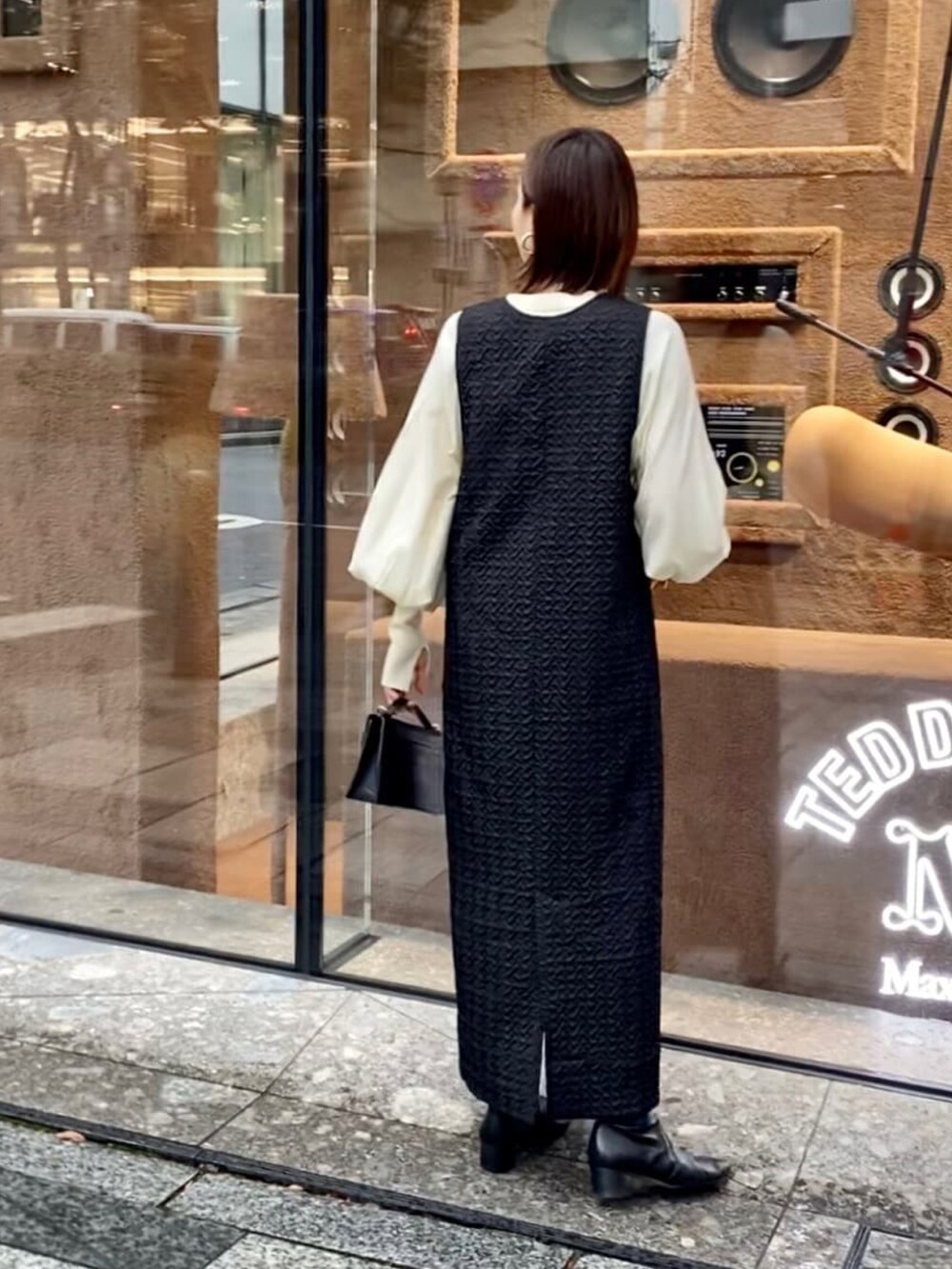 ブラック系のジャンパースカート、ホワイト系のニット/セーター、ブラック系のブーツを着用したレディースの秋コーディネートの3枚目の写真