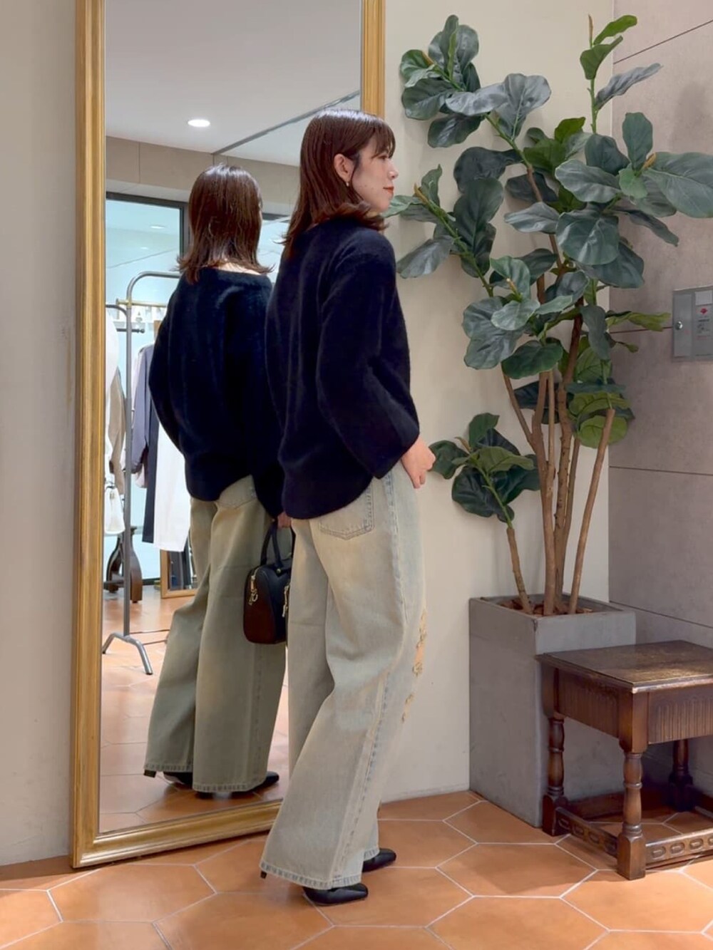 ブラック系のニット/セーター、ブラック系のボストンバッグ、ブルー系のデニムパンツを着用したレディースの秋コーディネートの2枚目の写真