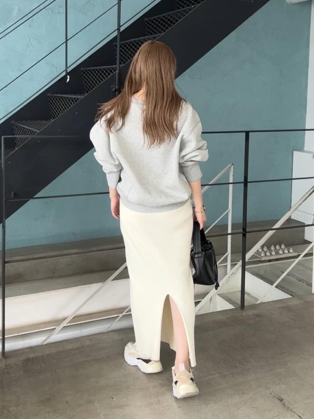 グレー系のスウェット、ホワイト系のスカート、ブラック系のハンドバッグを着用したレディースの秋コーディネートの3枚目の写真