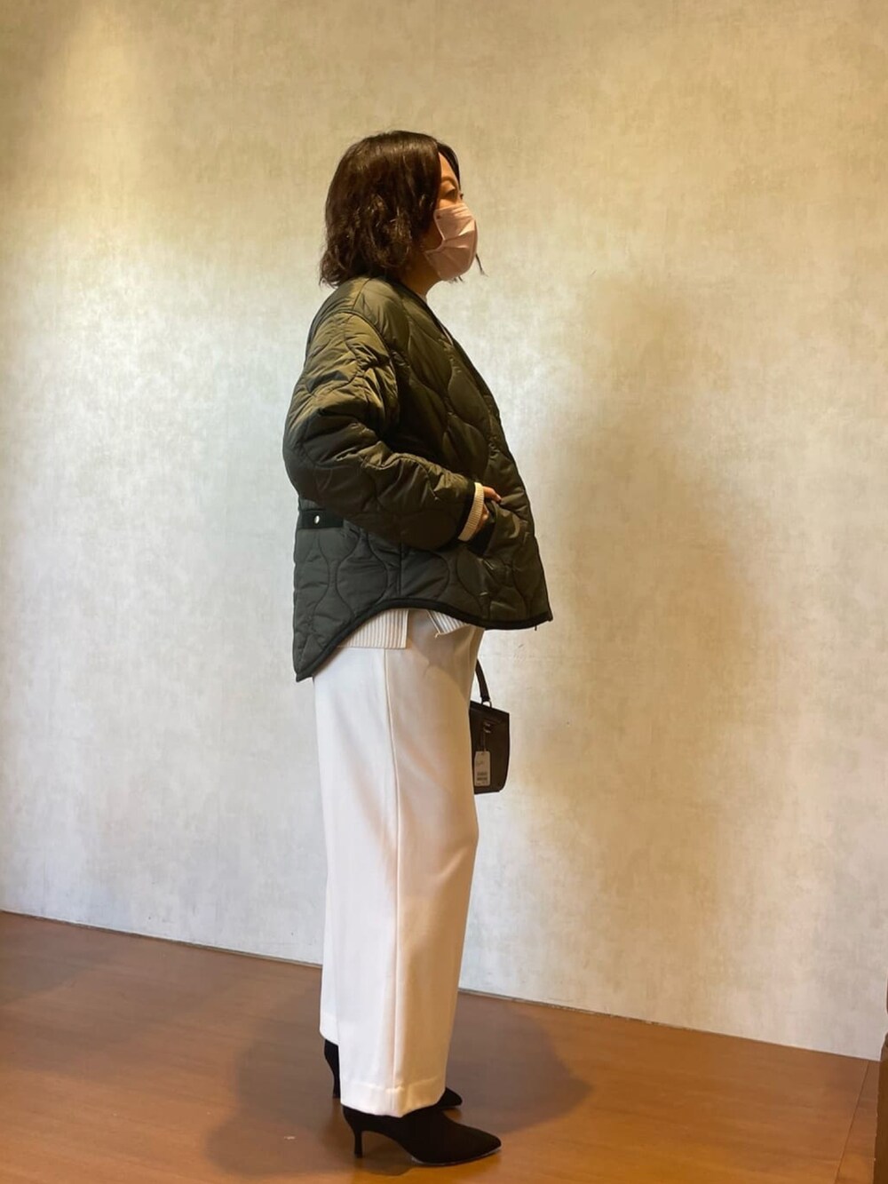 グリーン系のダウンジャケット/コート、ホワイト系のニット/セーター、ブラック系のブーツを着用したレディースの秋コーディネートの4枚目の写真