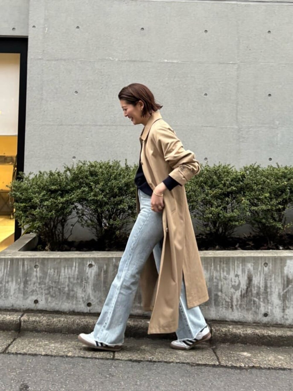 ブルー系のニット/セーター、ベージュ系のステンカラーコート、ブルー系のデニムパンツを着用したレディースの春コーディネートの3枚目の写真