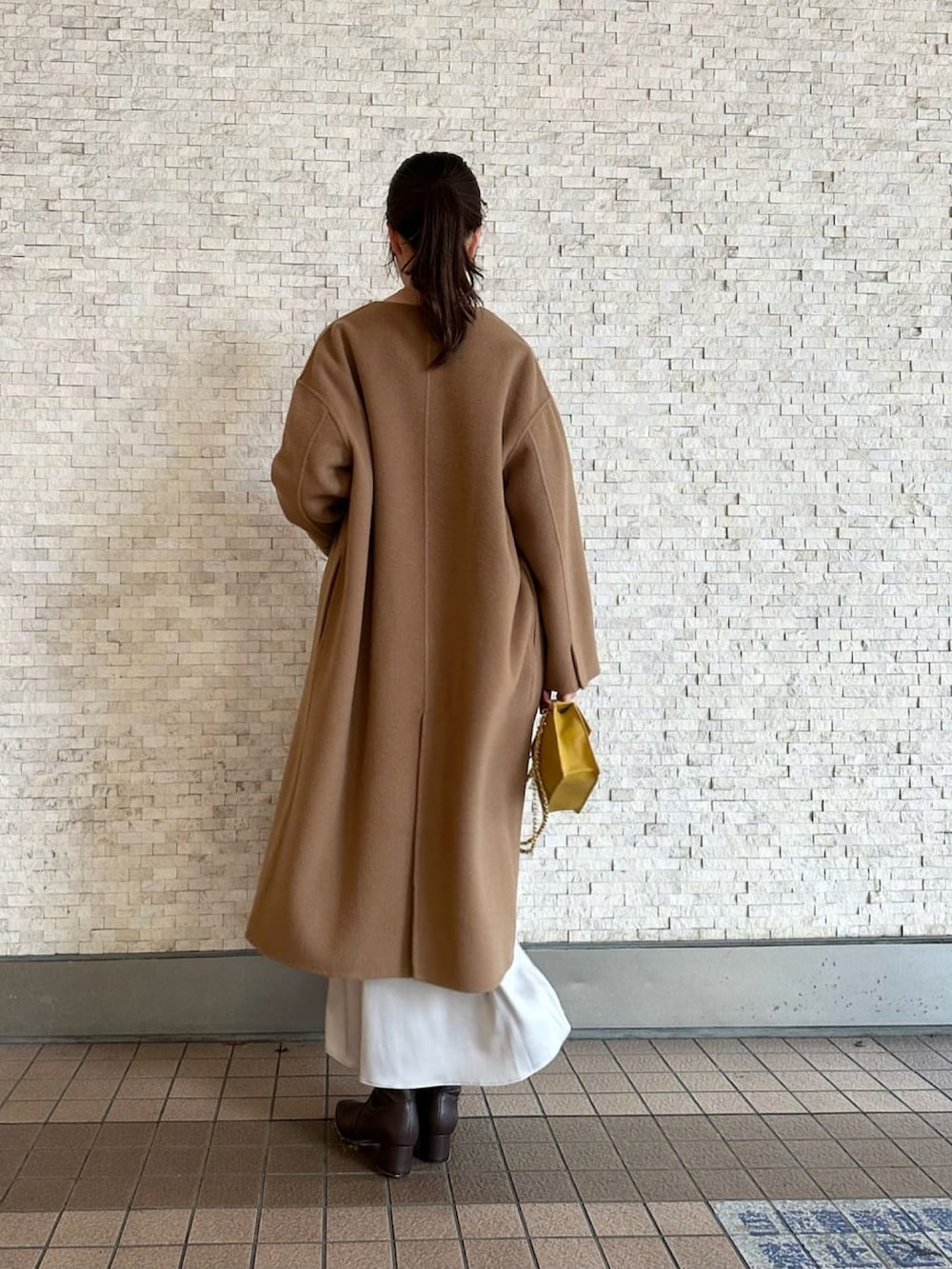 イエロー系のノーカラーコート、グレー系のニット/セーター、ブラウン系のブーツを着用したレディースの秋コーディネートの3枚目の写真