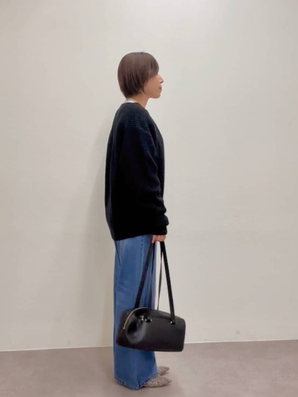 ブラック系のショルダーバッグ、グレー系のパンプス、ブルー系のデニムパンツを着用したレディースの秋コーディネートの4枚目の写真