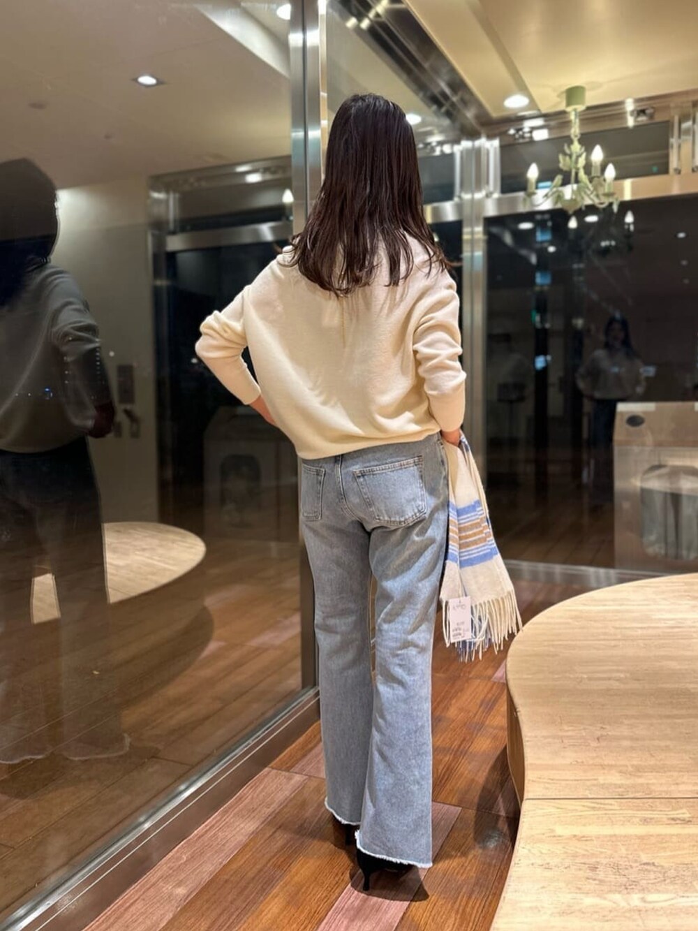 ブルー系のデニムパンツ、ホワイト系のニット/セーター、ホワイト系のトートバッグを着用したレディースの冬コーディネートの3枚目の写真