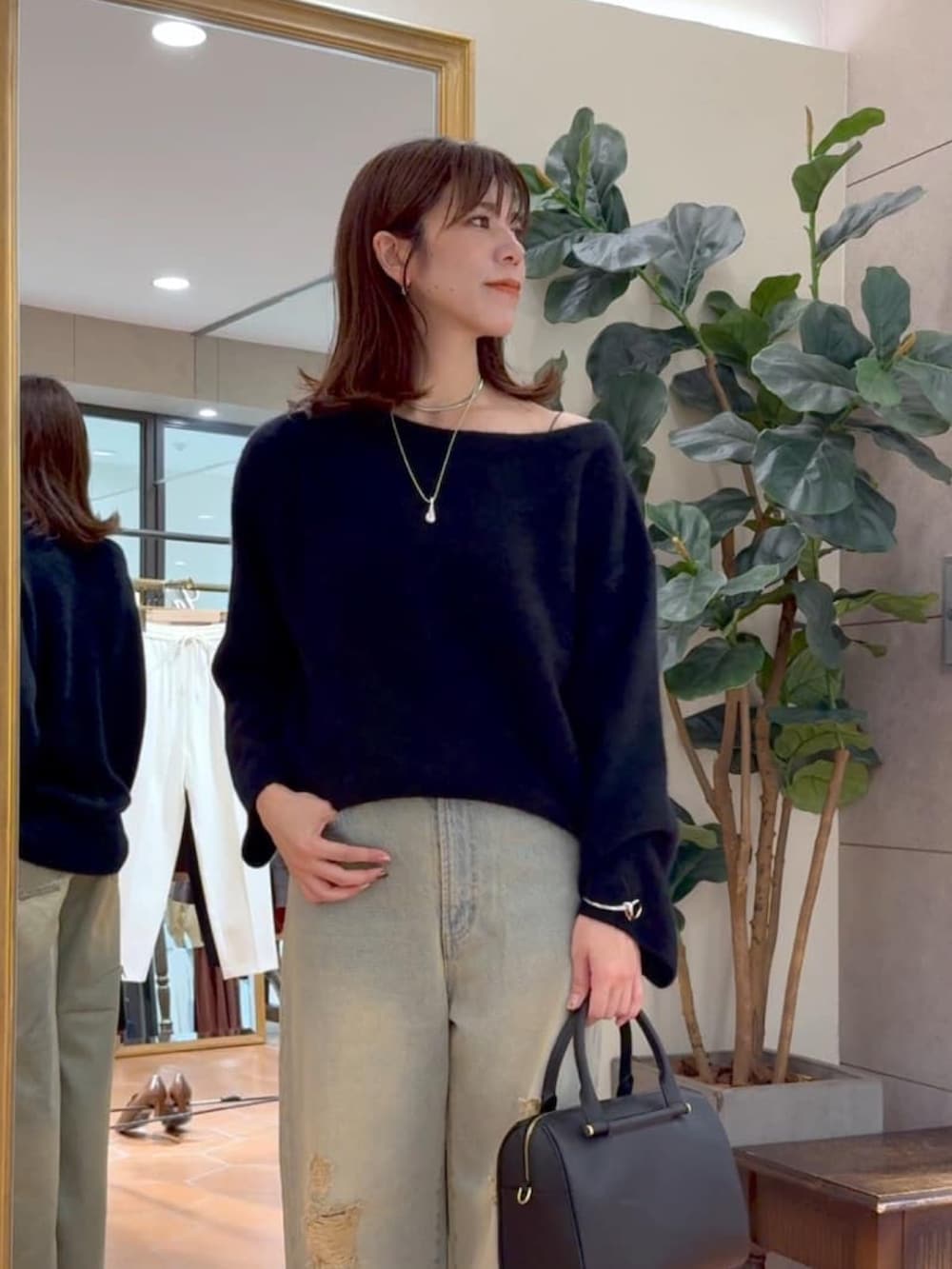 ブラック系のニット/セーター、ブラック系のボストンバッグ、ブルー系のデニムパンツを着用したレディースの秋コーディネートの4枚目の写真