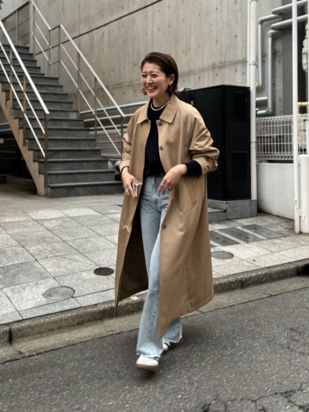 ブルー系のニット/セーター、ベージュ系のステンカラーコート、ブルー系のデニムパンツを着用したレディースの春コーディネートの2枚目の写真