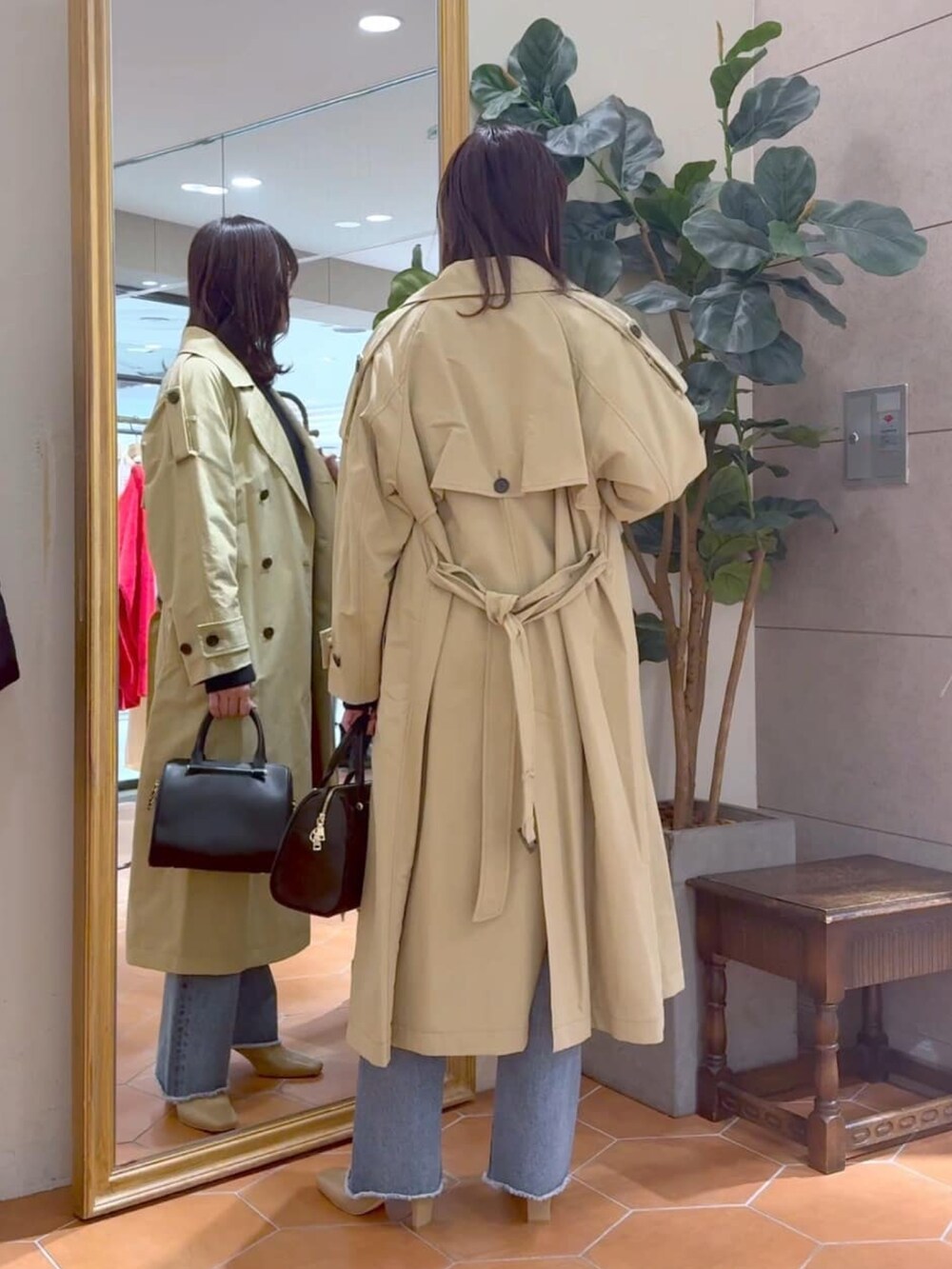 ベージュ系のトレンチコート、ブラック系のボストンバッグ、ブルー系のデニムパンツを着用したレディースの冬コーディネートの4枚目の写真