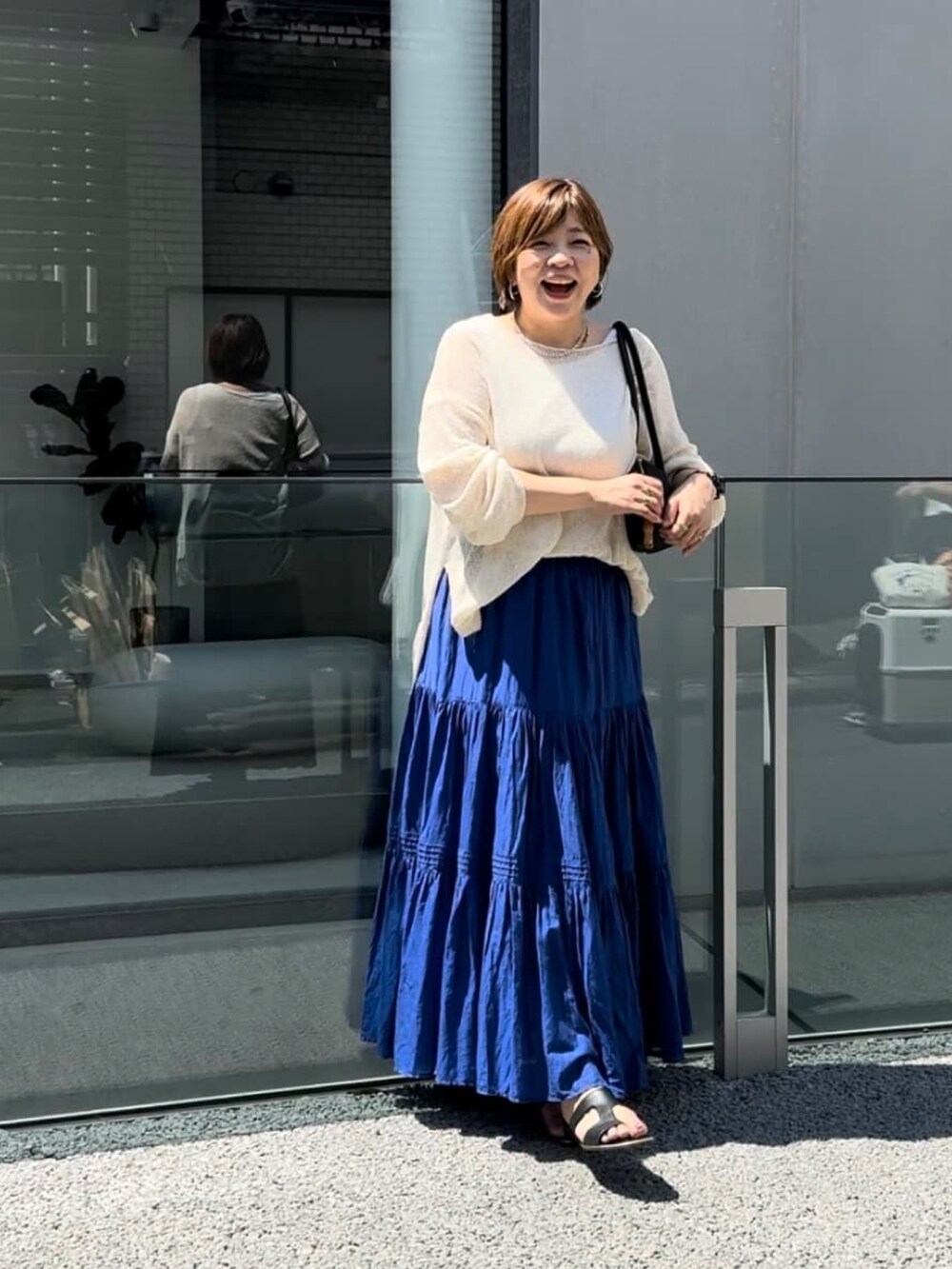 ブルー系のスカート、ホワイト系のニット/セーター、ブラック系のショルダーバッグを着用したレディースの春コーディネートの2枚目の写真