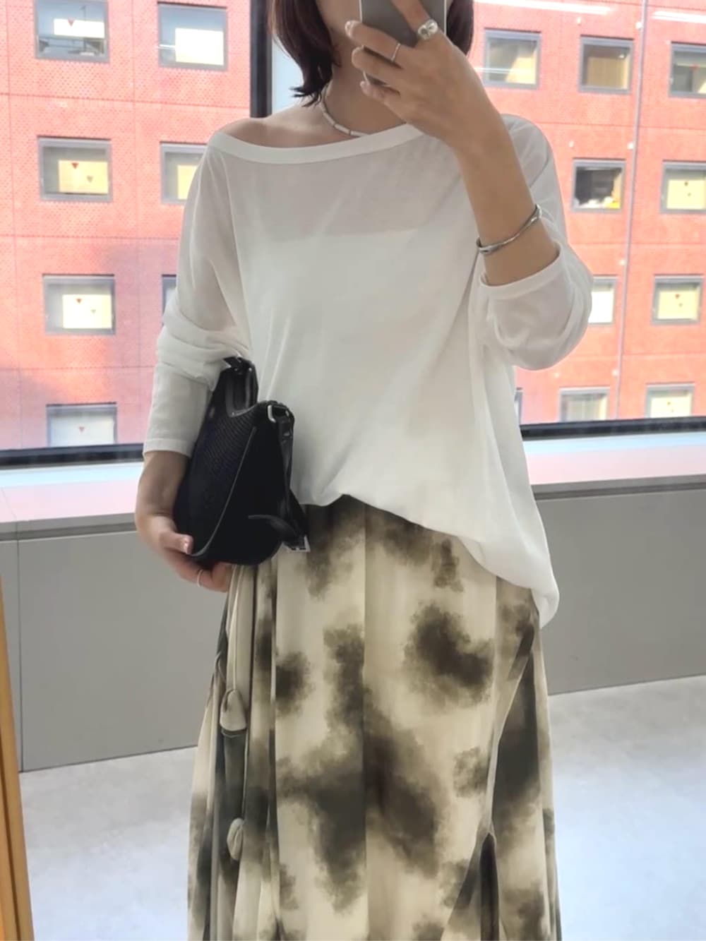 ブラック系のハンドバッグ、ベージュ系のスカート、ブラウン系のサンダルを着用したレディースの春コーディネートの2枚目の写真