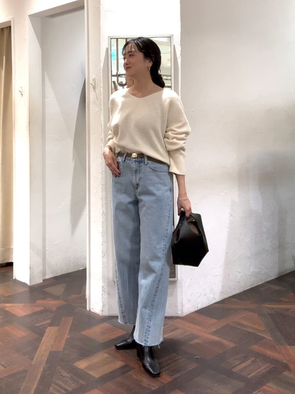 ホワイト系のニット/セーター、ブラック系のハンドバッグ、ブルー系のデニムパンツを着用したレディースの冬コーディネートの2枚目の写真