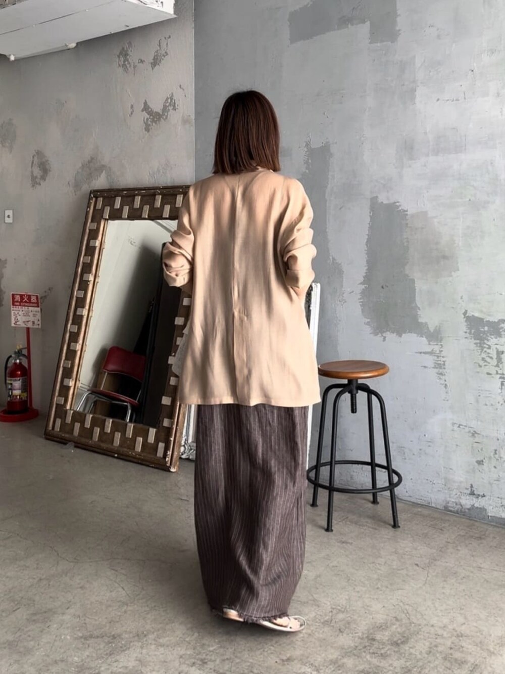 ブラック系のテーラードジャケット、ブラウン系のワンピース、シルバー系のサンダルを着用したレディースの春コーディネートの4枚目の写真