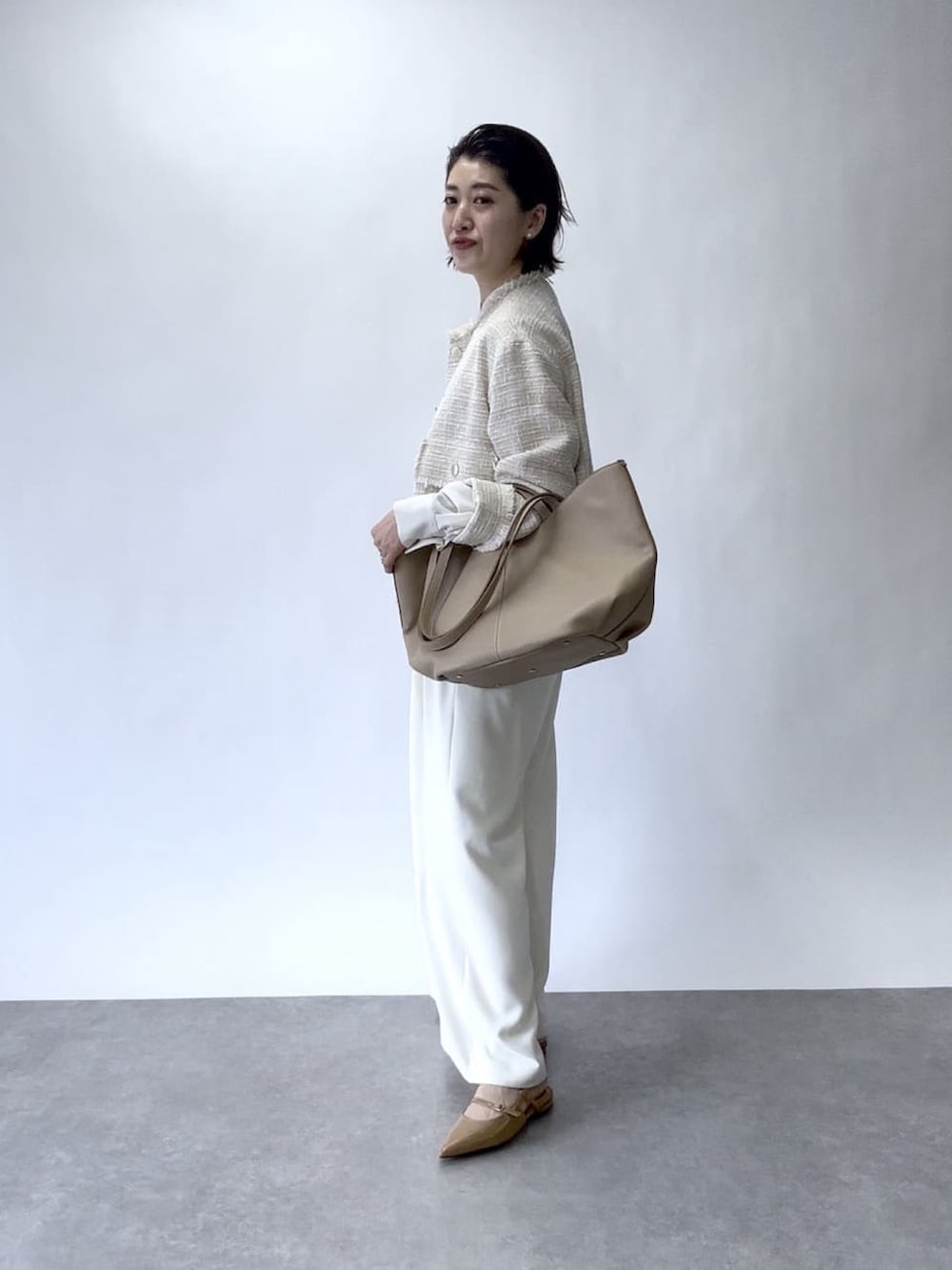 ホワイト系のスラックス、ベージュ系のノーカラージャケット、ベージュ系のトートバッグを着用したレディースの冬コーディネートの3枚目の写真