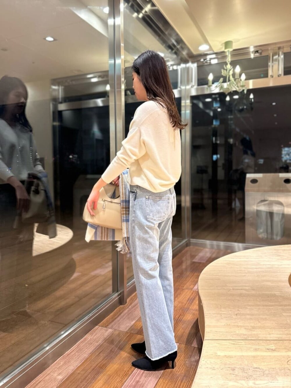 ブルー系のデニムパンツ、ホワイト系のニット/セーター、ホワイト系のトートバッグを着用したレディースの冬コーディネートの2枚目の写真