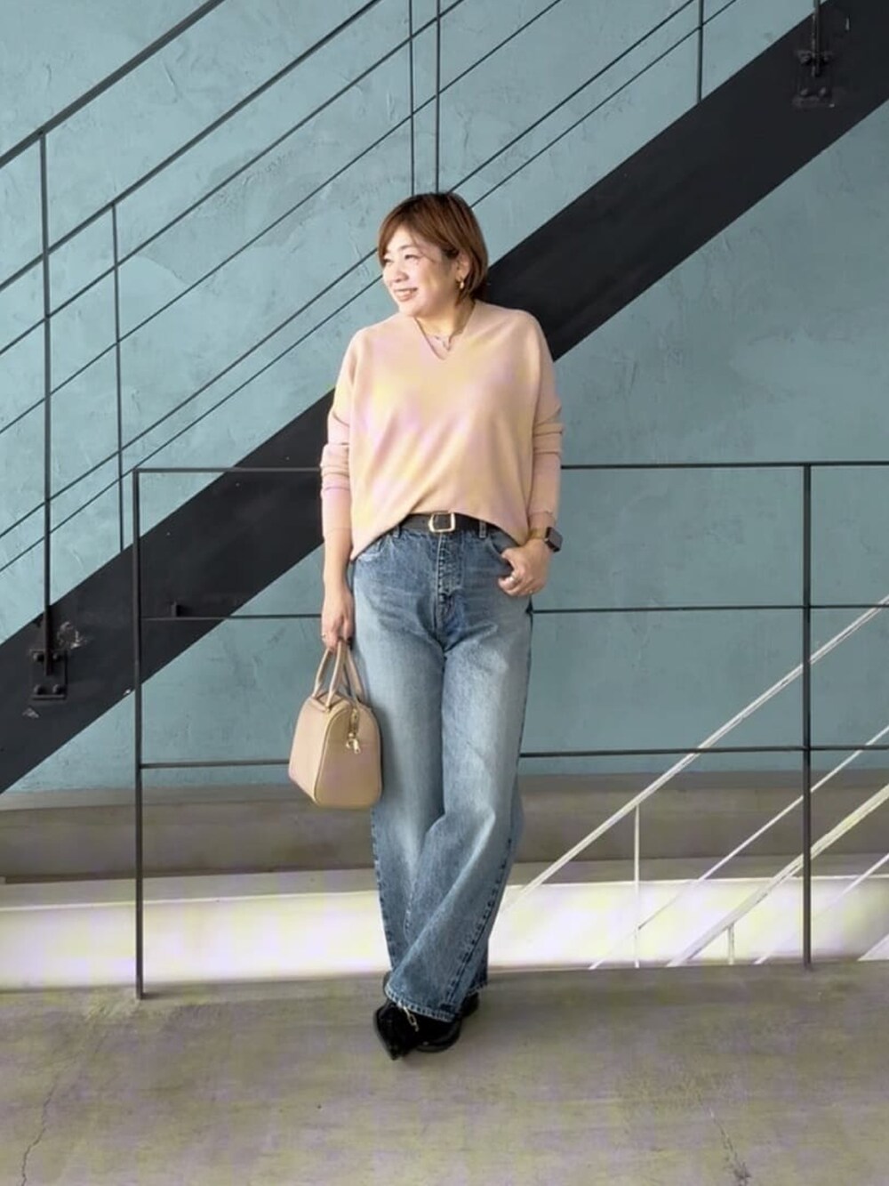 ピンク系のニット/セーター、ブルー系のデニムパンツ、ベージュ系のボストンバッグを着用したレディースの冬コーディネートの2枚目の写真