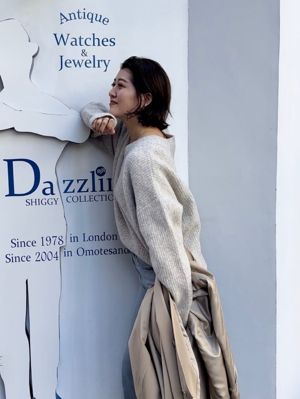 ベージュ系のステンカラーコート、ブルー系のデニムパンツ、グレー系のニット/セーターを着用したレディースの冬コーディネートの3枚目の写真