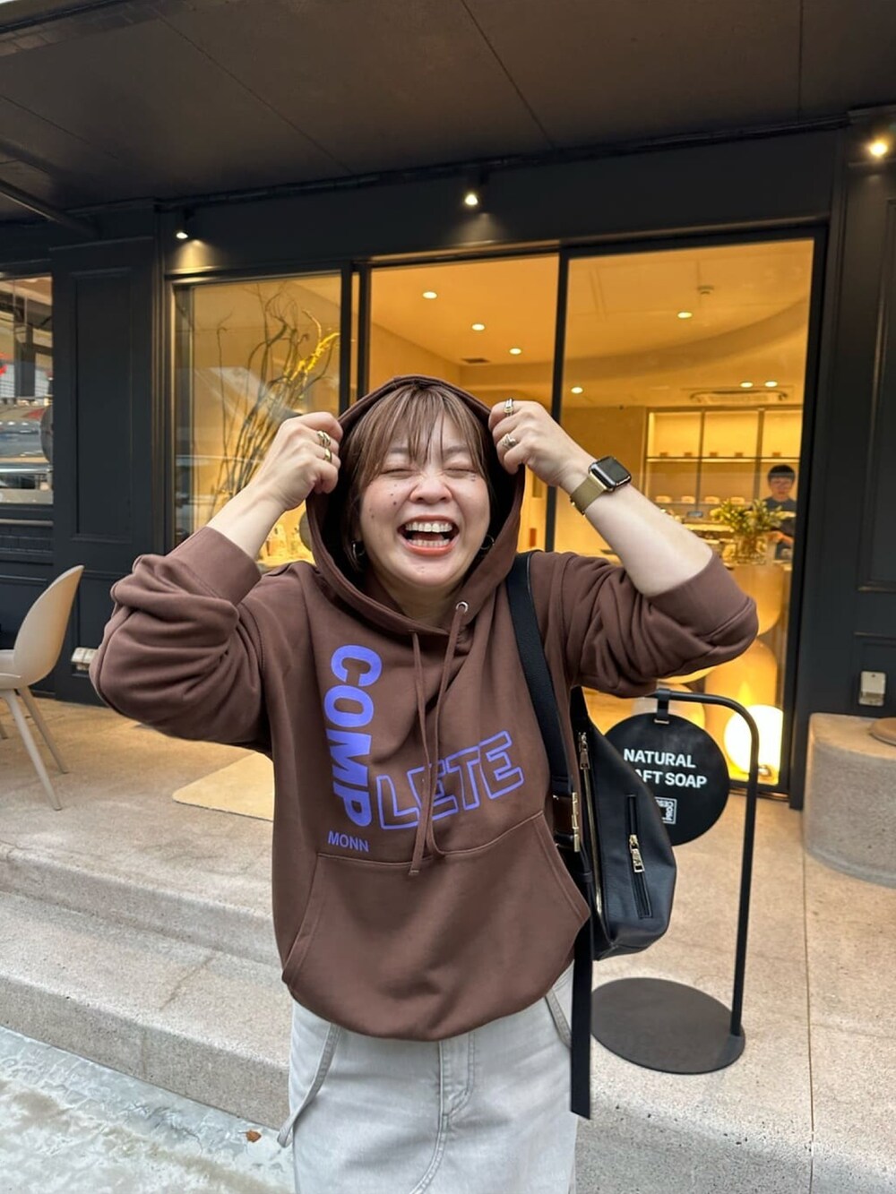 グレー系のデニムスカート、ブラック系のボディバッグ/ウエストポーチ、ブラウン系のパーカーを着用したレディースの秋コーディネートの2枚目の写真