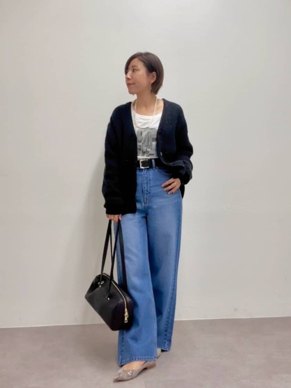 ブラック系のショルダーバッグ、グレー系のパンプス、ブルー系のデニムパンツを着用したレディースの秋コーディネートの2枚目の写真