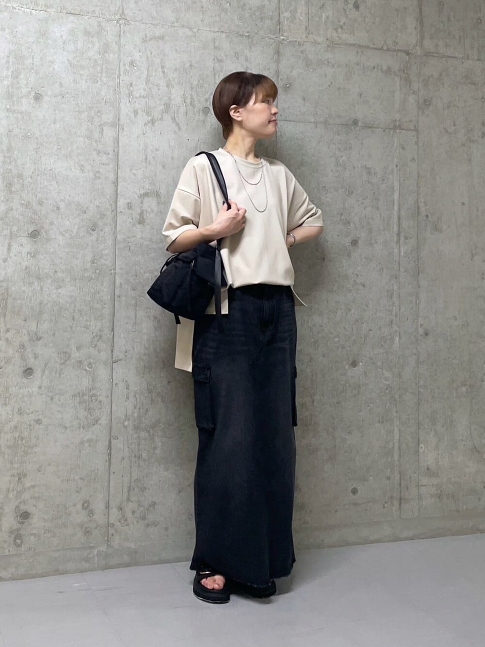 ベージュ系のTシャツ/カットソー、ブラック系のデニムスカート、ブラック系のサンダルを着用したレディースの夏コーディネートの2枚目の写真