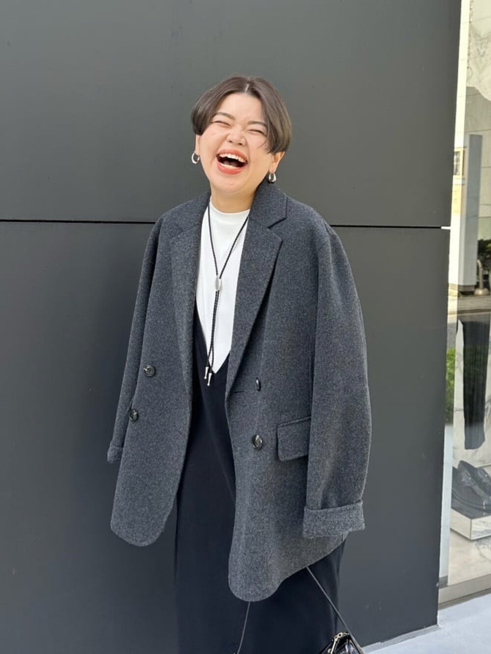 グレー系のテーラードジャケット、ブラック系のワンピース、ブラック系のショルダーバッグを着用したレディースの秋コーディネートの2枚目の写真