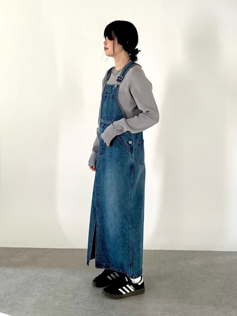 ブルー系のジャンパースカート、グレー系のニット/セーター、ブラック系のボディバッグ/ウエストポーチを着用したレディースの冬コーディネートの2枚目の写真