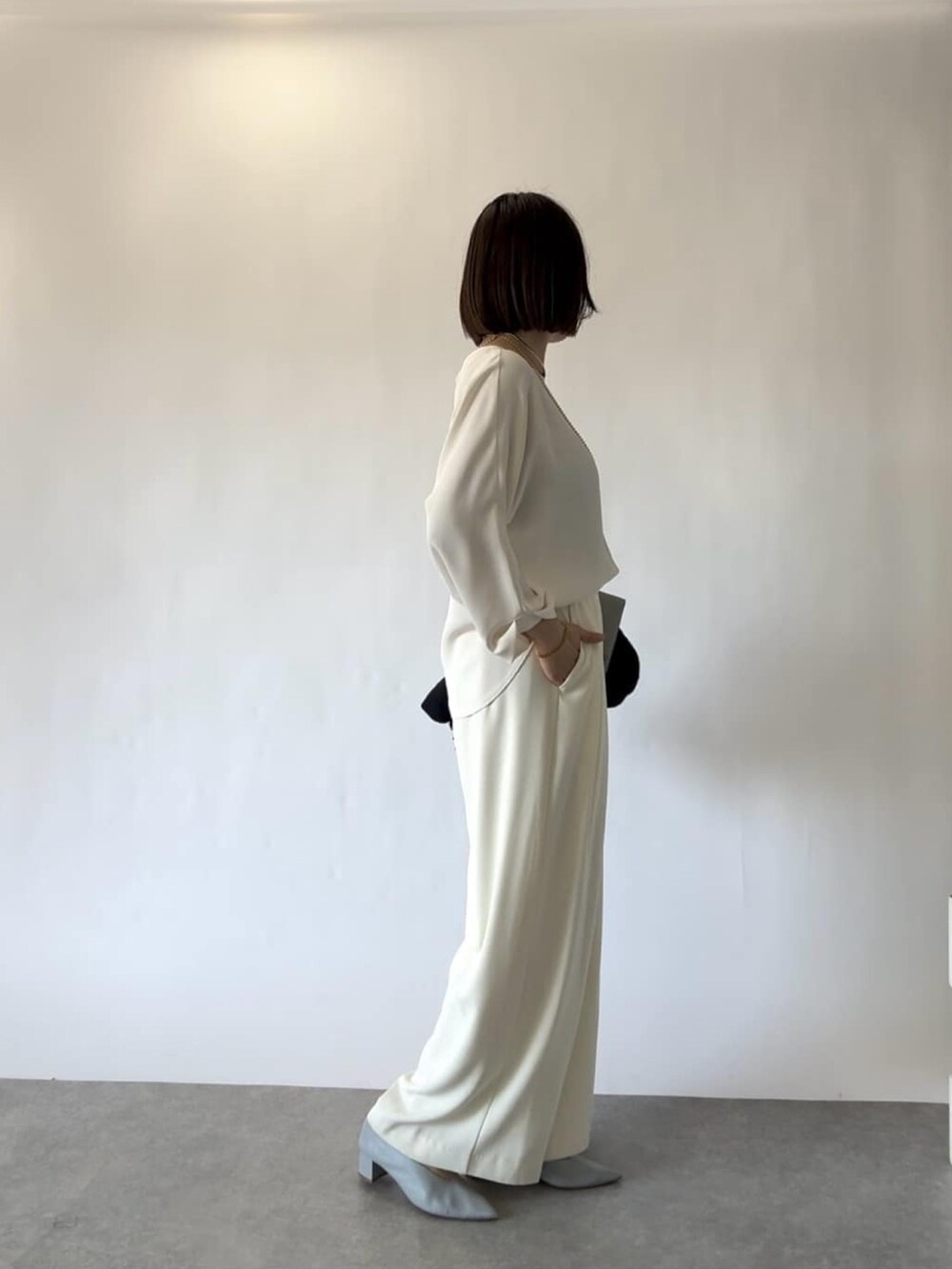 ホワイト系のスラックス、ブルー系のパンプス、ブルー系のショルダーバッグを着用したレディースの冬コーディネートの2枚目の写真