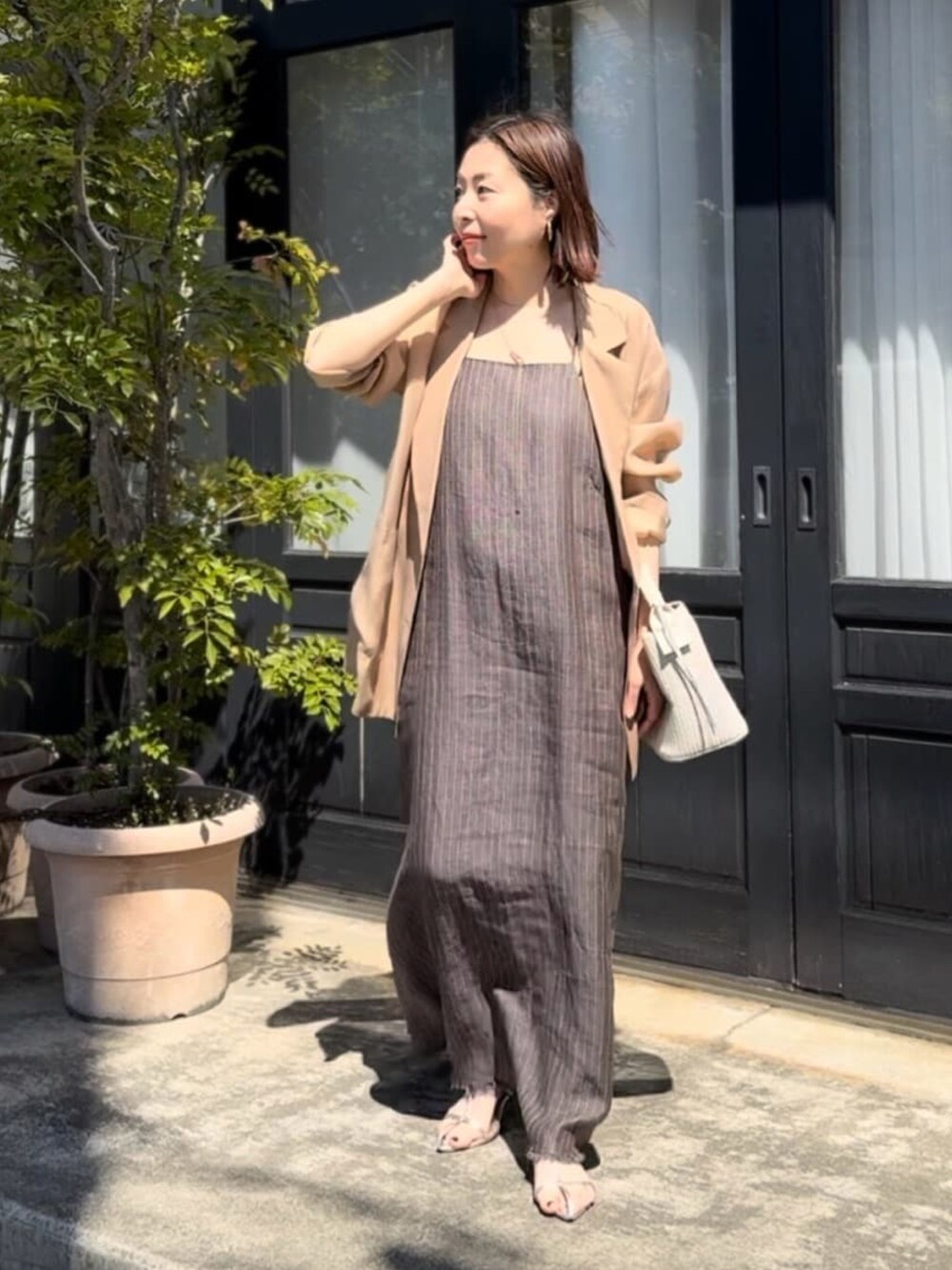 ブラック系のテーラードジャケット、ブラウン系のワンピース、シルバー系のサンダルを着用したレディースの春コーディネートの3枚目の写真