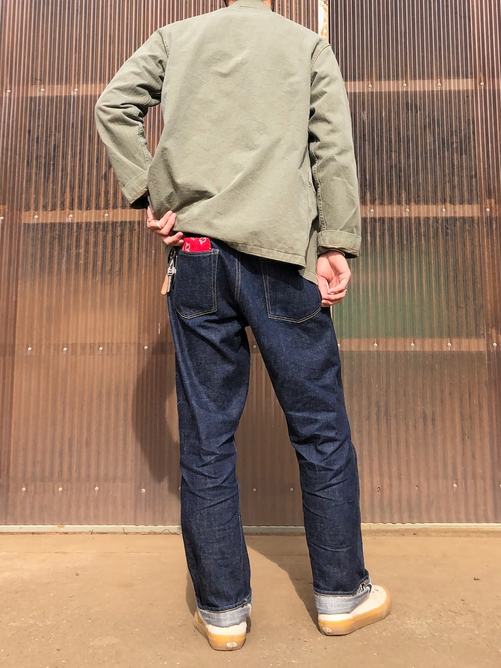 グリーン系のミリタリージャケット、グレー系のニット/セーター、ブルー系のデニムパンツを着用したメンズの春コーディネートの2枚目の写真