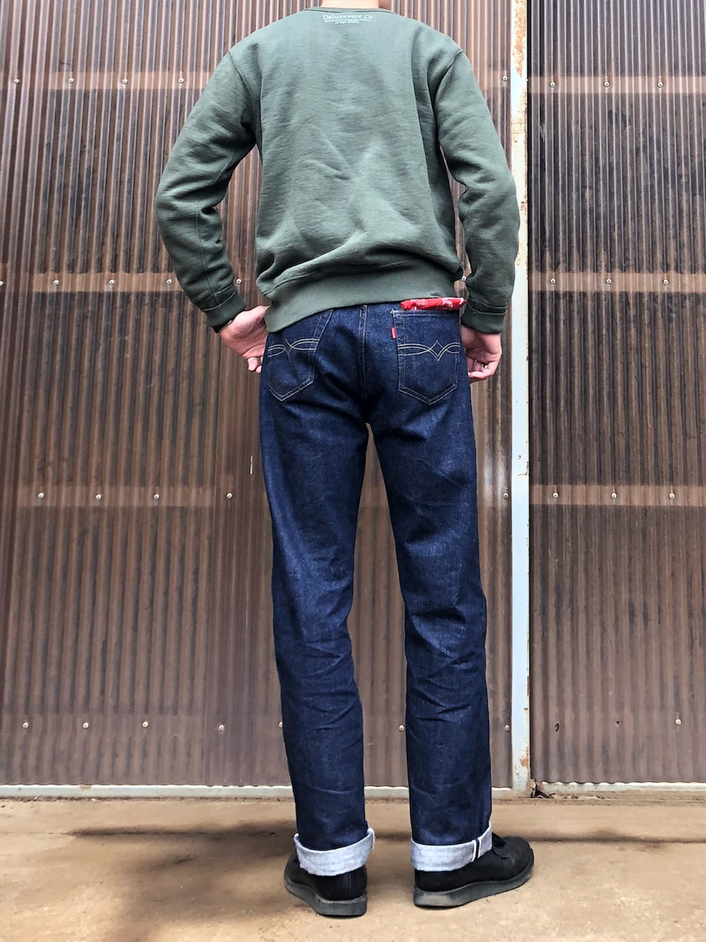 グリーン系のスウェット、ブルー系のデニムパンツ、ブラック系のブーツを着用したメンズの秋コーディネートの2枚目の写真