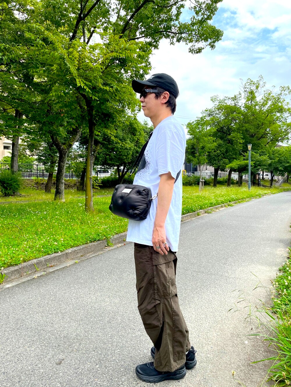 ブラック系のスニーカー、グリーン系のカーゴパンツ、ブラック系のショルダーバッグを着用したメンズの夏コーディネートの2枚目の写真