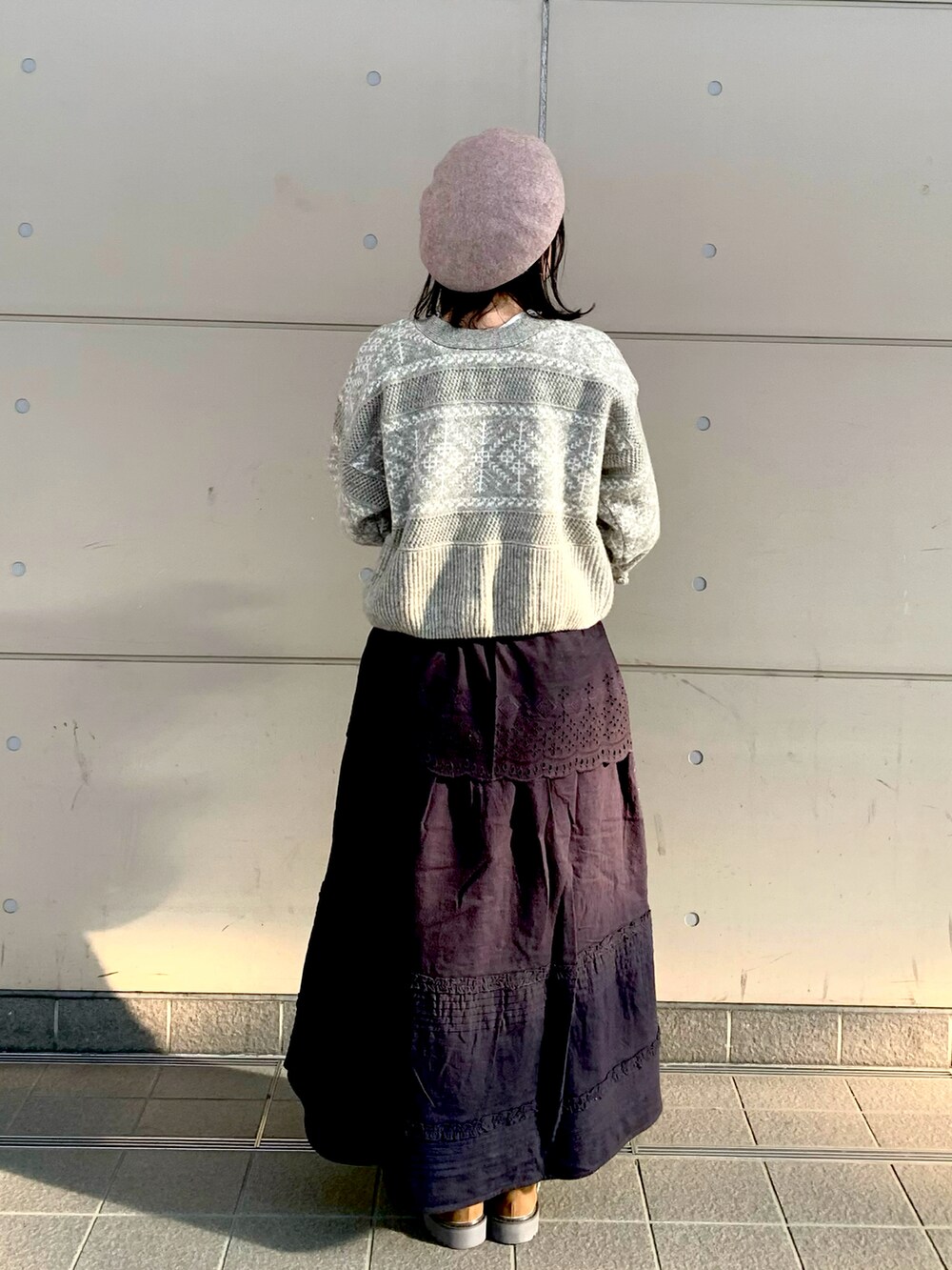 グレー系のニット/セーター、ブラック系のスカート、ベージュ系のTシャツ/カットソーを着用したレディースの秋コーディネートの2枚目の写真
