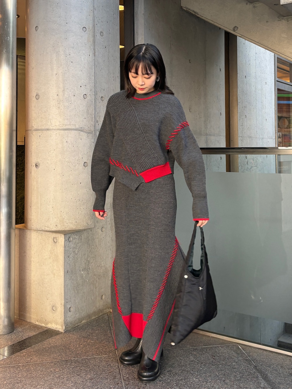 グレー系のニット/セーター、グレー系のスカート、ブラック系のハンドバッグを着用したレディースの秋コーディネートの2枚目の写真