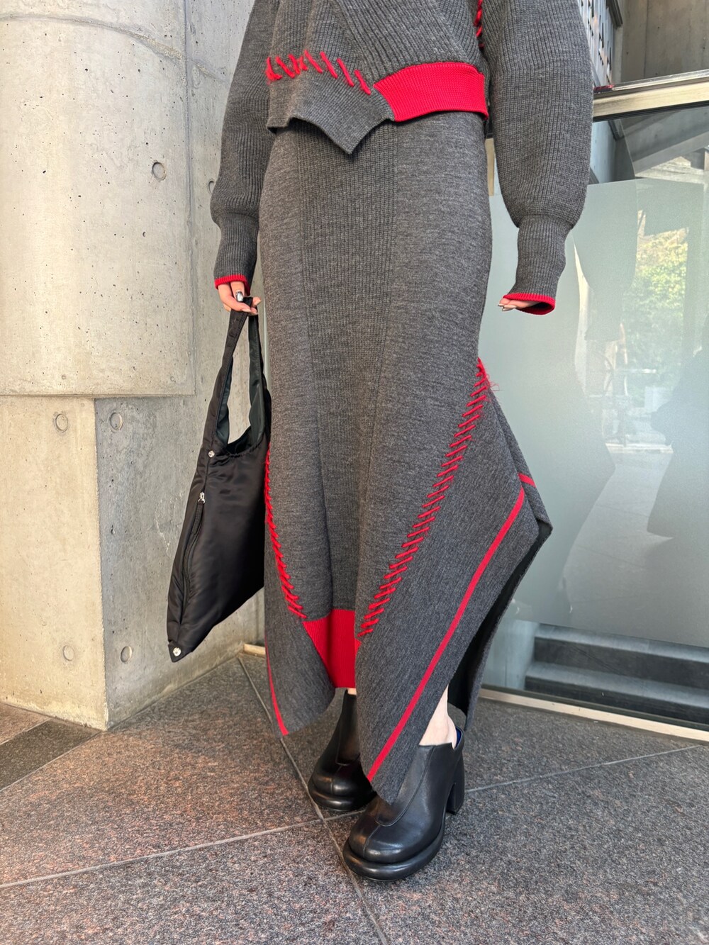 グレー系のニット/セーター、グレー系のスカート、ブラック系のハンドバッグを着用したレディースの秋コーディネートの5枚目の写真