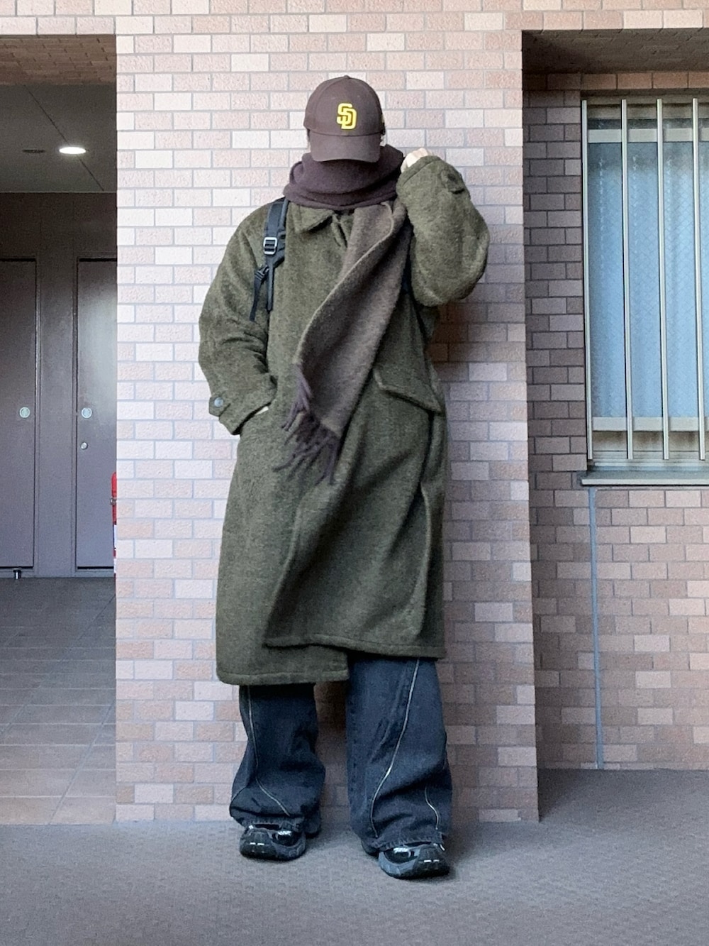 ブラック系のデニムパンツ、ブラウン系のステンカラーコート、ブラック系のスニーカーを着用したメンズの冬コーディネートの2枚目の写真