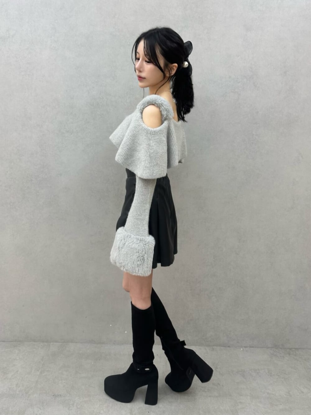 グレー系のニット/セーター、ブラック系のスカート、ブラック系のブーツを着用したレディースの秋コーディネートの3枚目の写真