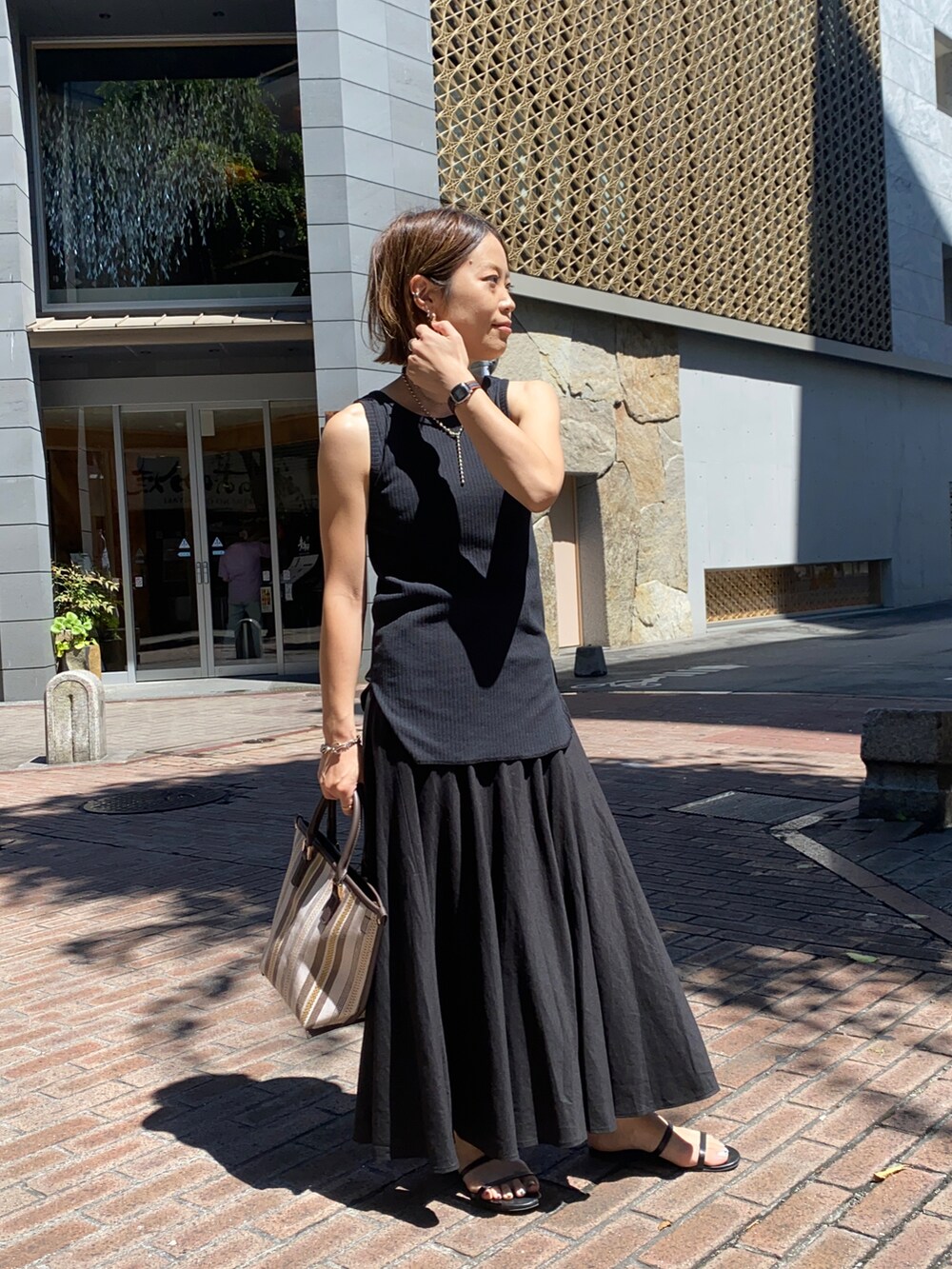 ブラック系のタンクトップ、ブラック系のスカート、ブラウン系のトートバッグを着用したレディースの夏コーディネートの2枚目の写真