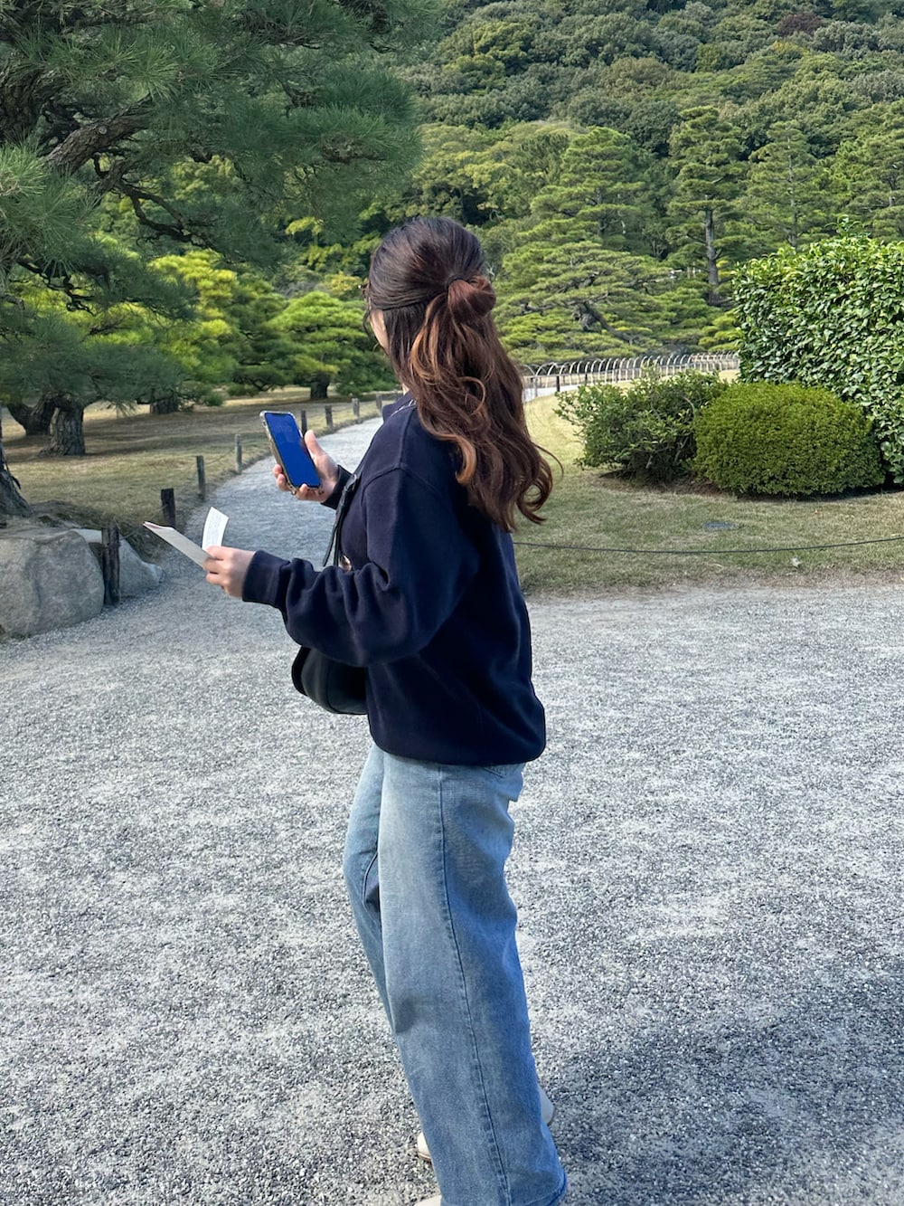 ブルー系のトップス、ブラック系のバッグ、ブルー系のデニムパンツを着用したレディースの秋コーディネートの2枚目の写真