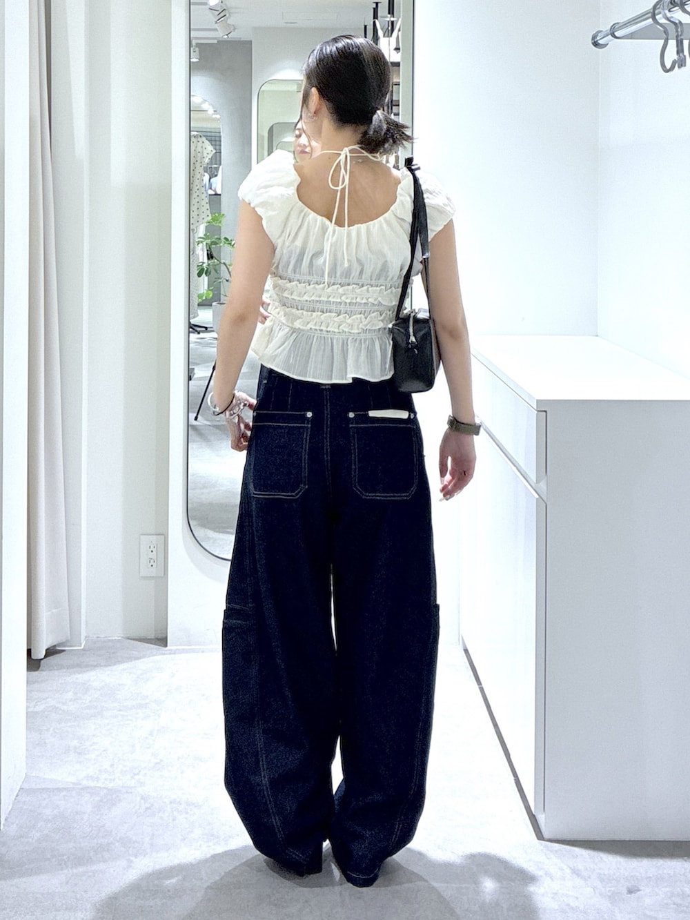ブルー系のデニムパンツ、ホワイト系のシャツ/ブラウス、ブラック系のショルダーバッグを着用したレディースの夏コーディネートの5枚目の写真