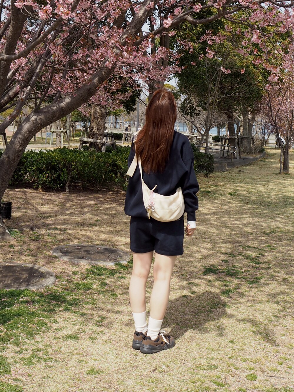 ブラウン系のスニーカー、ベージュ系のショルダーバッグ、ブルー系のトップスを着用したレディースの春コーディネートの2枚目の写真